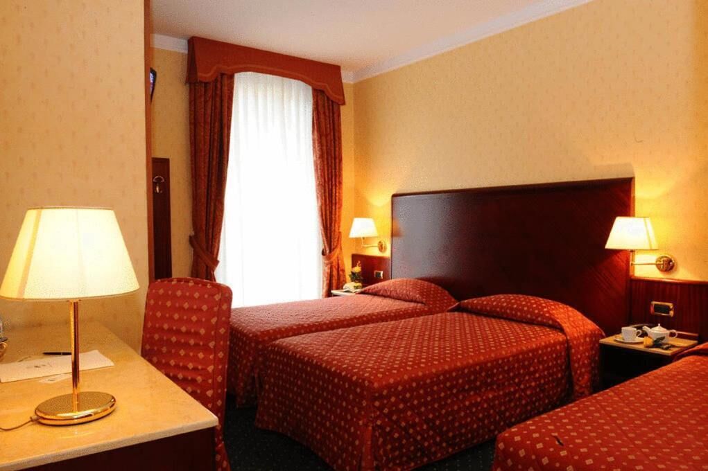 Une chambre d’hôtel avec deux lits, un bureau, une chaise et une fenêtre avec des rideaux.