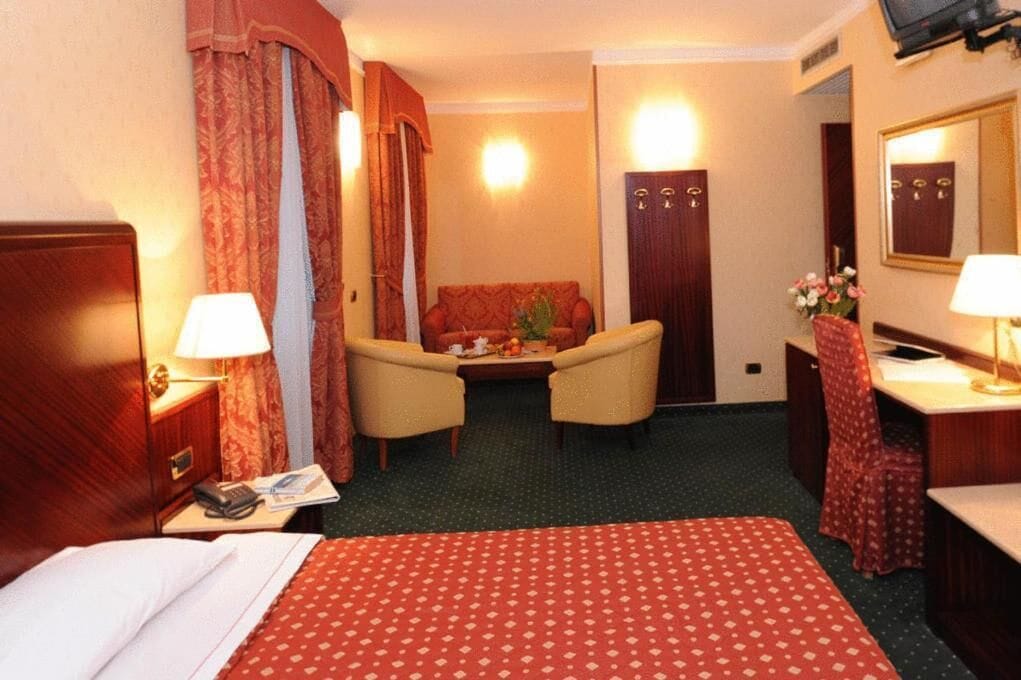Quarto de hotel com cama, escrivaninha, poltrona, sofá e televisão.