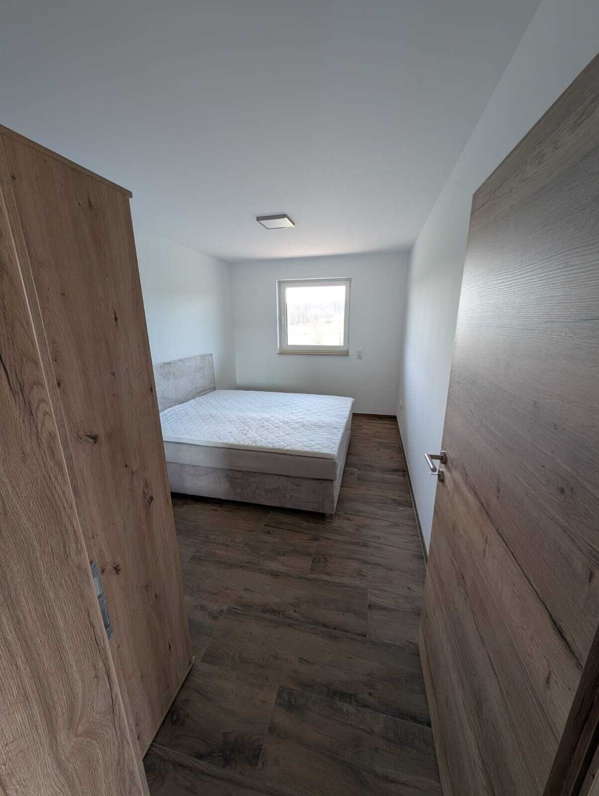 Un dormitorio con cama, ventana y piso de madera.