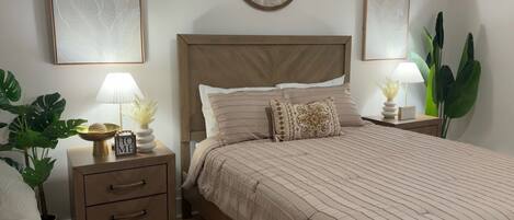 A bedroom with a bed, nightstands, a lamp, and a potted plant.