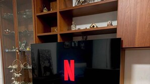 Un mobile in legno contenitore con un televisore a schermo piatto che mostra il logo di Netflix, un portafortuna e diversi oggetti decorativi.