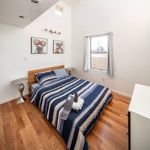 A bedroom with a bed, two bedside tables, a window, and artwork on the wall.