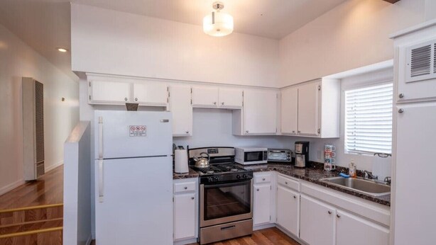 A modern kitchen with white cabinetry, a stainless steel refrigerator, a built-in oven, a microwave, and a gas stove. - Bright 2 Bed Venice Loft (Los Angeles)