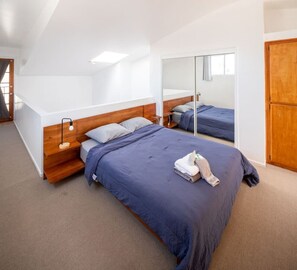 A modern bedroom with a large bed, a bedside table, a mirror, and a wardrobe.