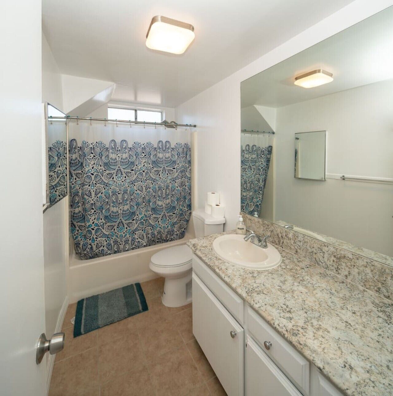 A bathroom with a shower curtain, toilet, sink, and mirror.