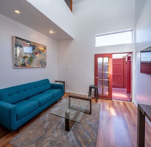 A modern living room with a blue sofa, a glass coffee table, and a painting on the wall. - Bright 2 Bed Venice Loft (Los Angeles)