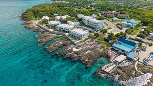 Eine Luftaufnahme eines Küstenresorts mit mehreren Gebäuden, einer felsigen Küstenlinie und klarem türkisfarbenem Wasser.