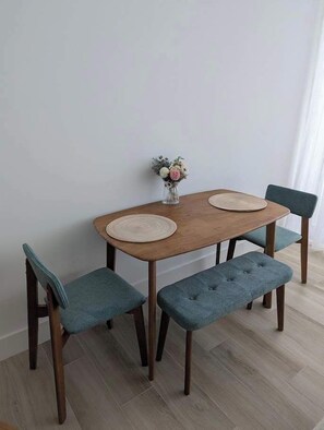 Una mesa de comedor con dos sillas y un banco, un florero con flores y una pared de color claro.