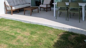 Ein moderner Außenbereich mit einer Couch, Sesseln und einem Tisch, mit einer Glastür, die zu einem Balkon führt.