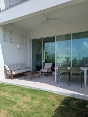Un área exterior moderna para el esparcimiento, con un sofá, sillas y una mesa, que cuenta con una puerta de cristal que da a un balcón.