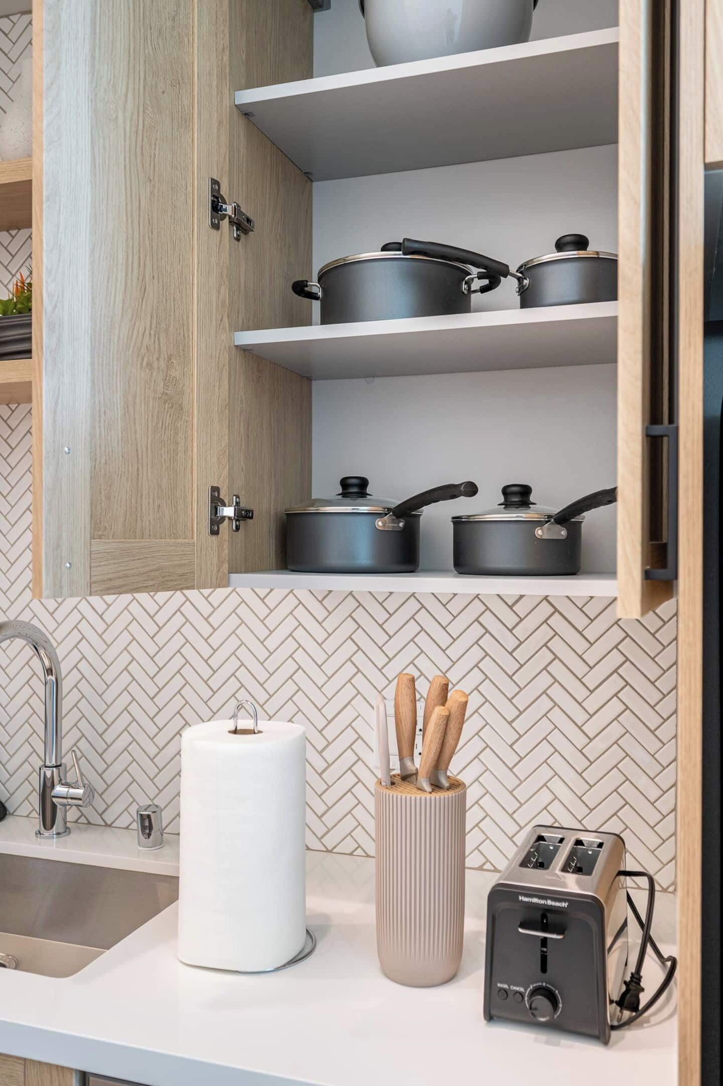 A kitchen with wooden cabinets, a herringbone tile backsplash, a stainless steel sink, a roll of paper towels, a spice rack, and a toaster.