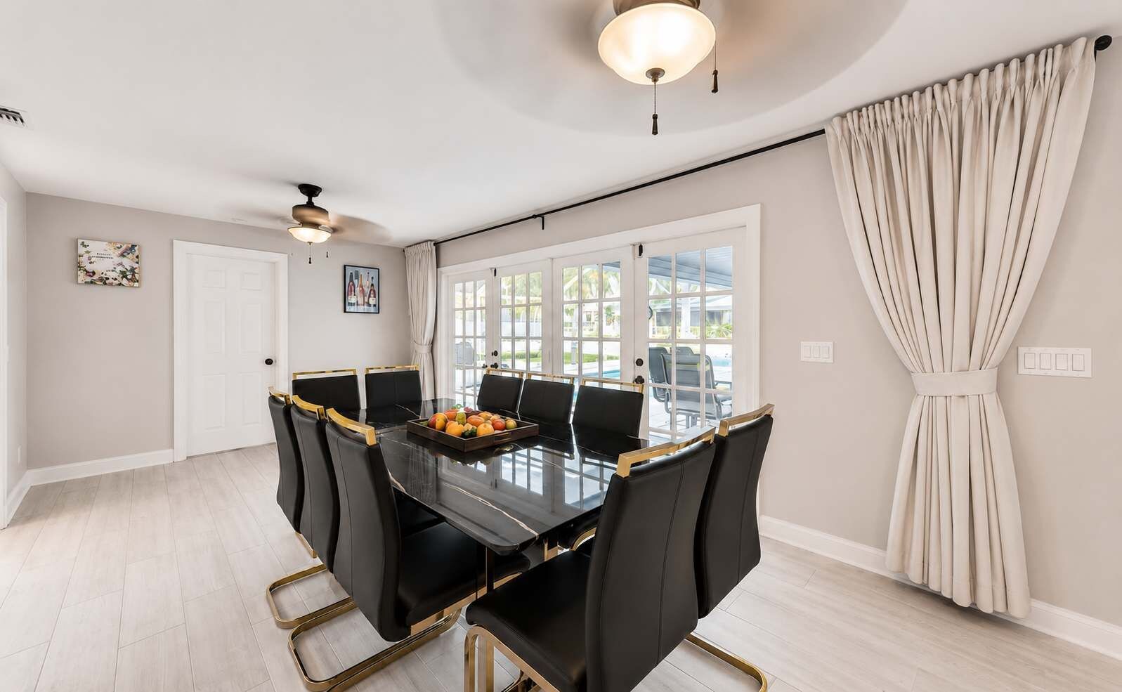 A dining room with a black table and chairs, a fruit bowl, and a view of the outdoors.