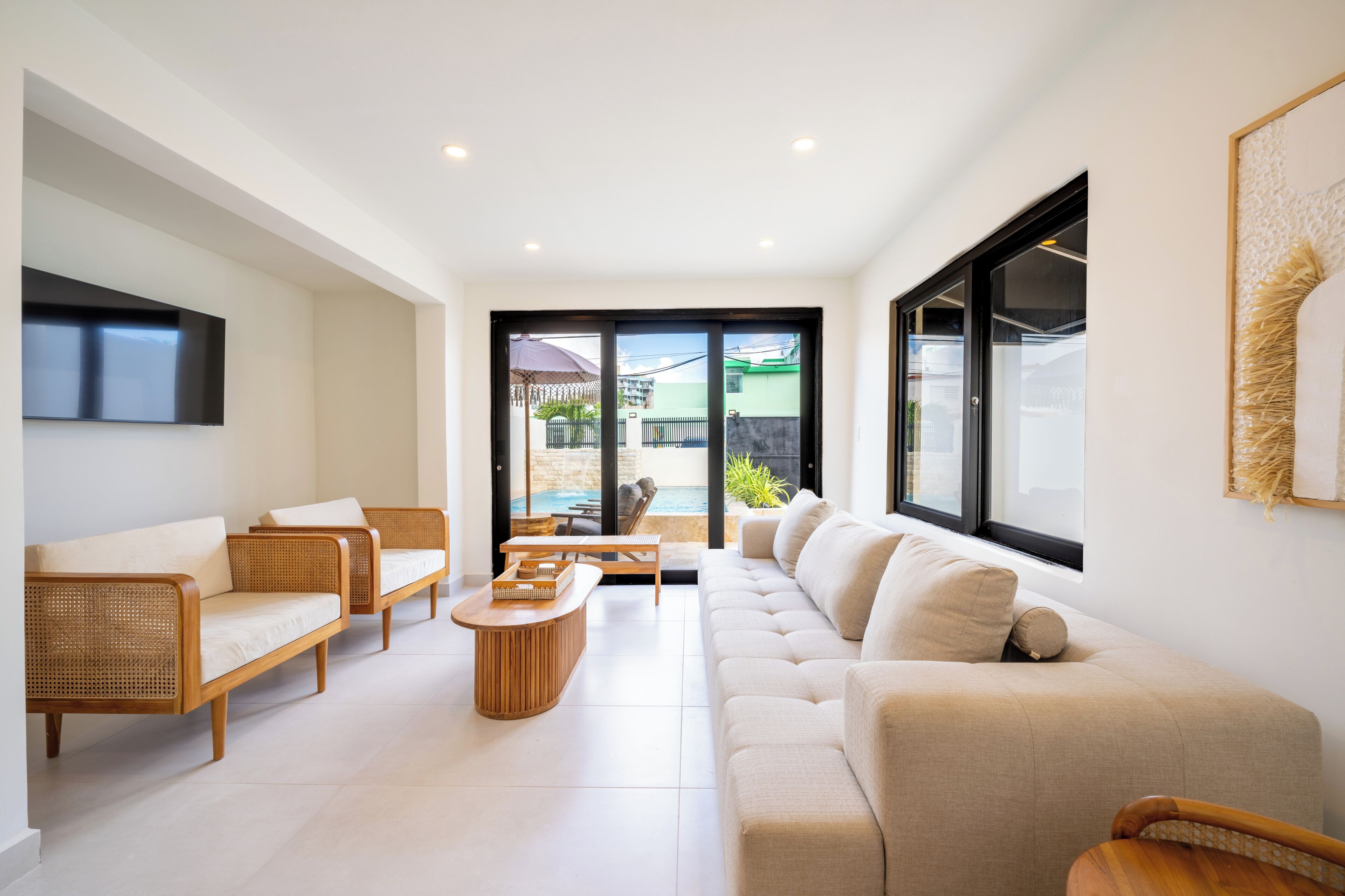 A modern living room with a sofa, chairs, and a coffee table. There is a view of a swimming pool through the glass door.