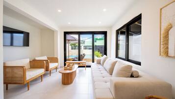 A modern living room with a sofa, chairs, and a coffee table. There is a view of a swimming pool through the glass door.