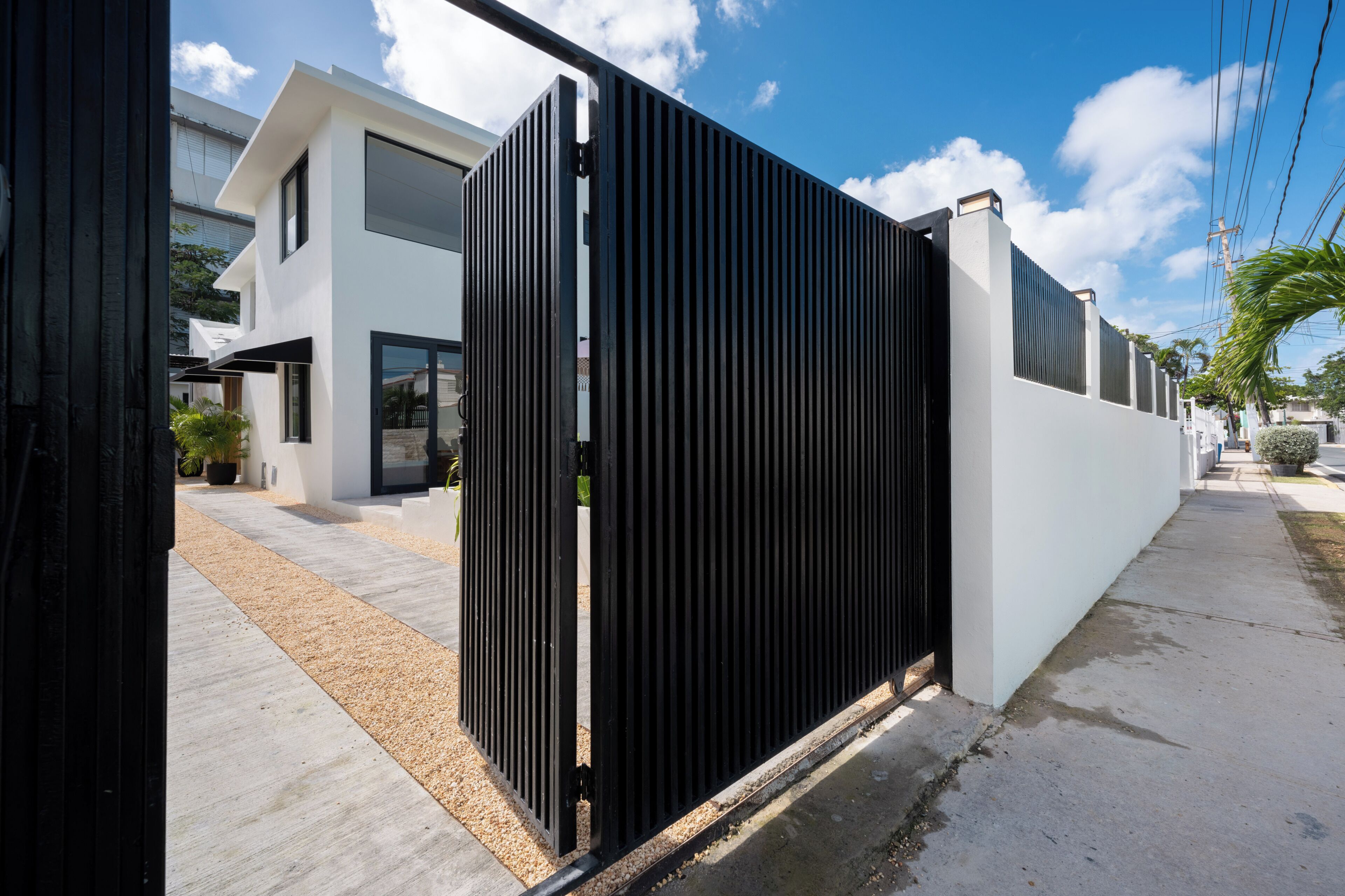A modern house with a black metal gate, a white exterior, and a paved driveway.