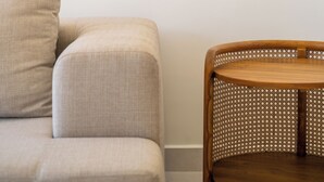 Huoneessa on beigenvärinen sohva, puinen ruokapöytä ja seinälle ripustettu taideteos.