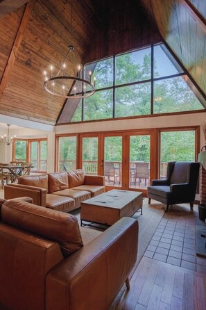 A spacious living area with a high ceiling, large windows, and a chandelier. - Crocketts: Pond Views, Seasonal Waterfall, Hot Tub (Logan)