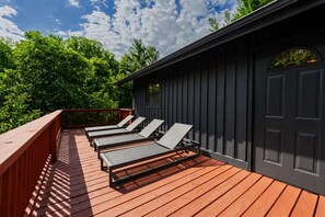 Eine Terrasse mit vier Liegestühlen, einem Hollerleger und einem dunklen Gebäude mit einer Tür und einem Fenster.