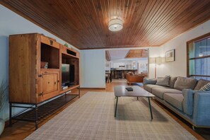Ein Wohnzimmer mit einem Holzschrank, einer Couch, einem Couchtisch und einer Küche im Hintergrund.