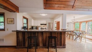 Una cocina amplia con una isla de madera y taburetes, un comedor con mesa y sillas, y ventanas grandes que brindan luz natural.