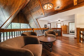 A spacious loft bedroom with a sloped ceiling, wooden beams, and a balcony with a railing. - Crocketts: Pond Views, Seasonal Waterfall, Hot Tub (Logan)