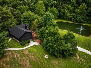 A house with a dark roof, surrounded by lush greenery and a pond with a fountain. - Crocketts: Pond Views, Seasonal Waterfall, Hot Tub (Logan)
