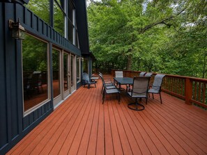 A wooden deck with outdoor furniture, large windows, and a view of trees. - Crocketts: Pond Views, Seasonal Waterfall, Hot Tub (Logan)