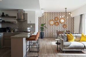A modern kitchen with a central island, bar stools, and a dining area with a sofa and cushions. - Amazing Apt W/ Pool In Regatta Living By YellowKey (Santo Domingo)