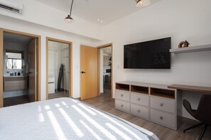 A modern bedroom with a bed, a TV mounted on the wall, and a desk with drawers. - Amazing Apt W/ Pool In Regatta Living By YellowKey (Santo Domingo)