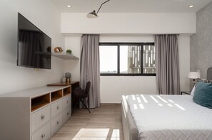 A modern bedroom with a bed, a desk, a chair, a TV, and a window with curtains. - Amazing Apt W/ Pool In Regatta Living By YellowKey (Santo Domingo)