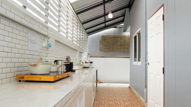A kitchen with white tiled walls, a wooden floor, and a countertop with cooking appliances. - 4BR Family Home • Garden & Sala • Sleeps 9 • Near Airport (Nong Phueng)
