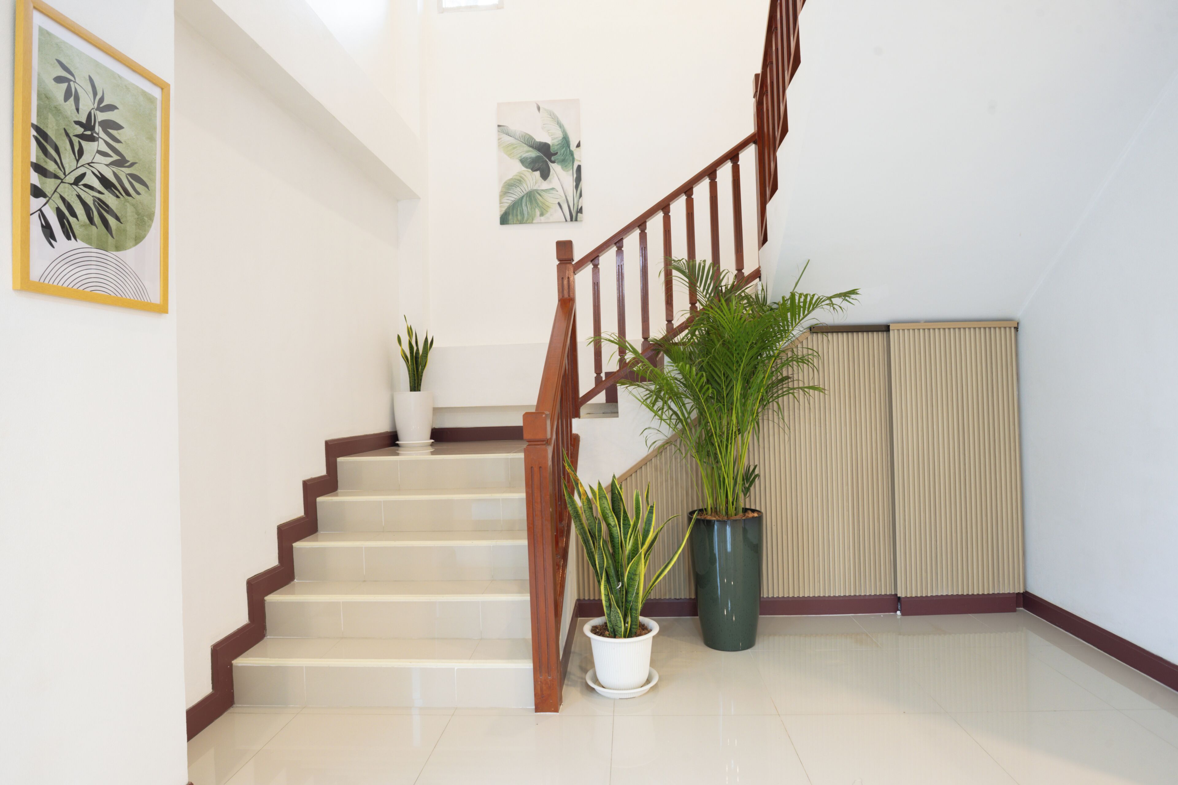 A staircase with wooden railings, white walls, and two potted plants.