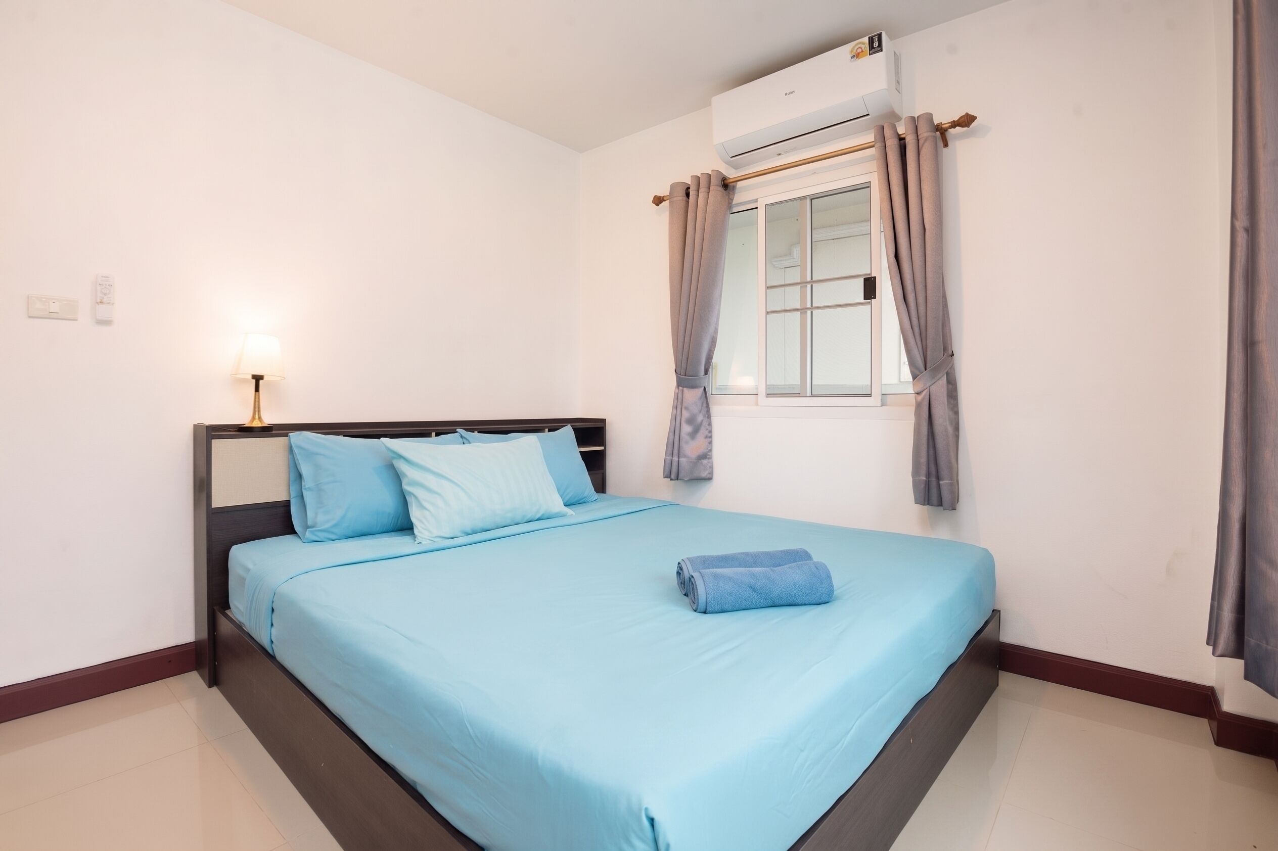 A bedroom with a bed, a nightstand, a lamp, an air conditioning unit, and a window with curtains.