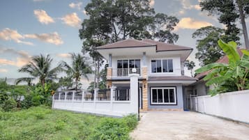 A two-story house with a balcony, surrounded by greenery and trees.