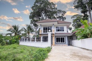 A two-story house with a balcony, surrounded by greenery and trees. - 4BR Family Home • Garden & Sala • Sleeps 9 • Near Airport (Nong Phueng)