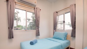 A single bed with a blue mattress and pillows, a window with curtains, and an air conditioning unit on the wall. - 4BR Family Home • Garden & Sala • Sleeps 9 • Near Airport (Nong Phueng)