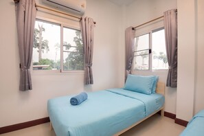A single bed with a blue mattress and pillows, a window with curtains, and an air conditioning unit on the wall. - 4BR Family Home • Garden & Sala • Sleeps 9 • Near Airport (Nong Phueng)