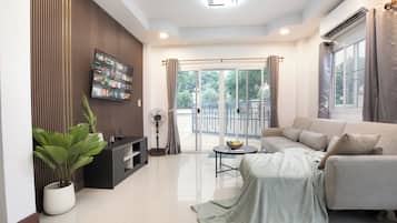 A modern living room with a flat-screen TV, a sofa, a coffee table, and a potted plant.