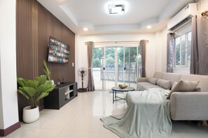 A modern living room with a flat-screen TV, a sofa, a coffee table, and a potted plant. - 4BR Family Home Sleeps 9 • Garden & Sala • 15 Min to Old City (Nong Phueng)