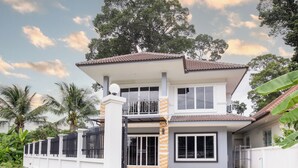 A two-story house with a balcony, large windows, and a gated entrance. - 4BR Family Home • Garden & Sala • Sleeps 9 • Near Airport (Nong Phueng)