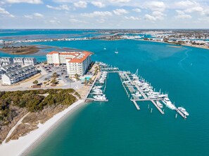 An aerial view of a marina with boats docked, a hotel with multiple floors, and a beach area.