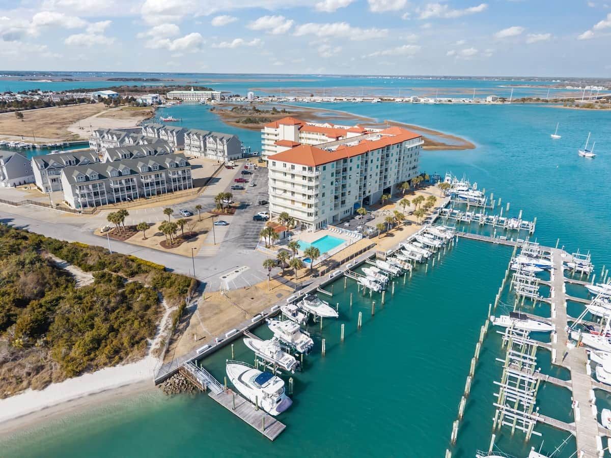 Een jachthaven met aan wal liggende boten, een hotel met zwembad en een strand.