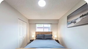 A bedroom with a wooden bed, two bedside lamps, a window, and a door. - Spacious 3BR/2BA Family Home in Delta | Sleeps 12 (Delta)