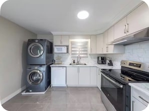 Une cuisine compacte équipée d’un lave-linge et d’un sèche-linge intégrés, d’un four à micro-ondes et d’une cuisinière.