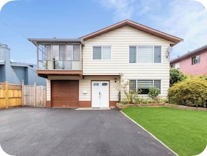 Une maison à deux étages avec un garage, une porte d’entrée et un petit jardin devant la maison, avec une pelouse et un arbuste.
