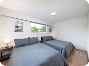 A room with two beds, a nightstand with a lamp, and a window with a view of greenery. - Spacious 3BR/2BA Family Home in Delta | Sleeps 12 (Delta)