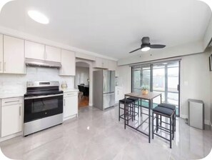 A modern kitchen with stainless steel appliances, a dining area with bar stools, and a view through large windows.