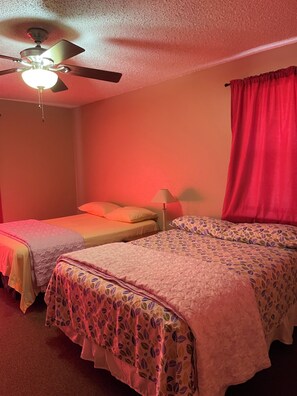 A bedroom with two beds, a ceiling fan, and a red curtain.