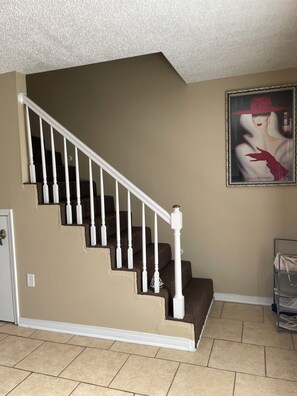 A staircase with white balusters and brown steps, leading to a landing with a beige wall and a framed artwork.