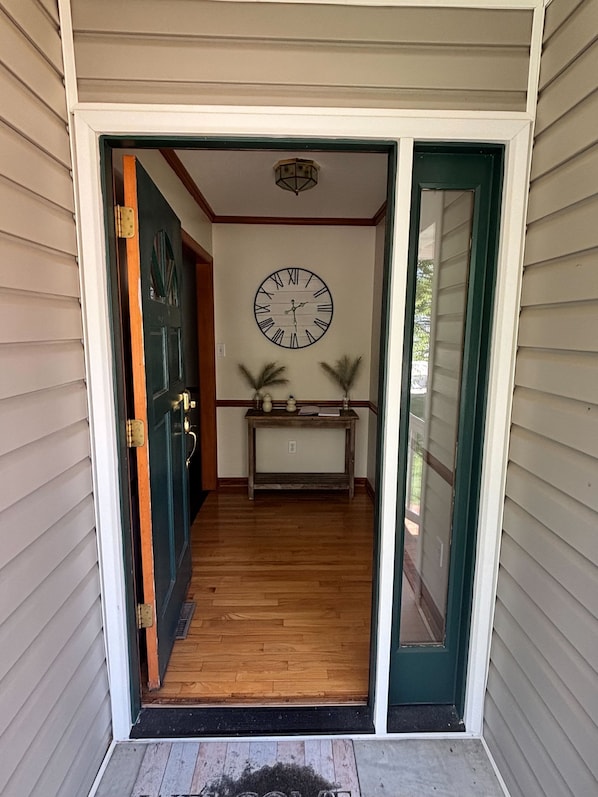 A hallway with a wooden floor, a clock on the wall, and a door on the left.